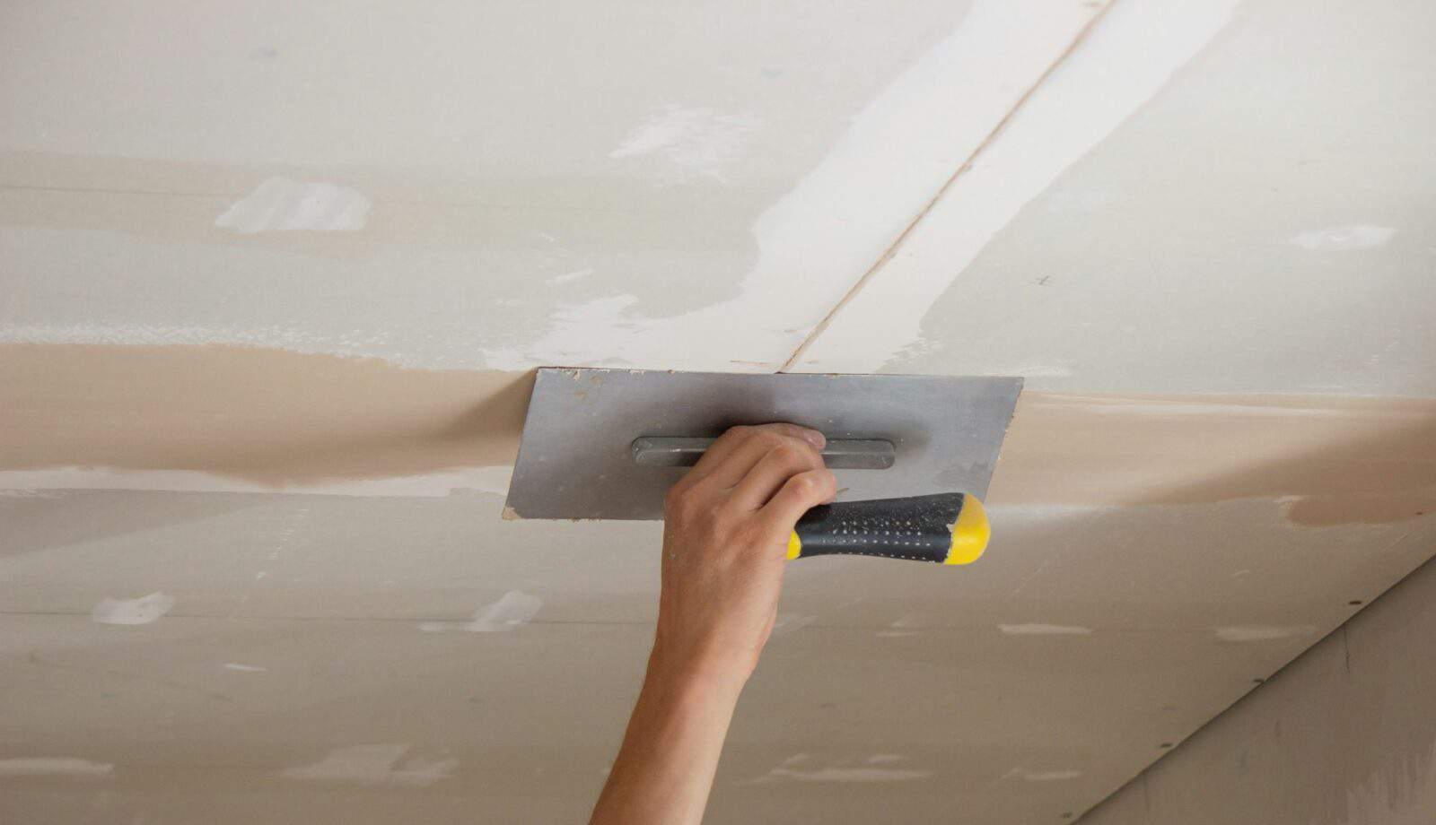 A man puts putty on a plasterboard ceiling. Putty for the joints of plasterboard sheets