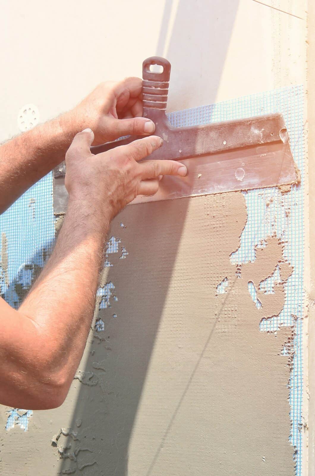 Hands of an old manual worker with wall plastering tools renovating house