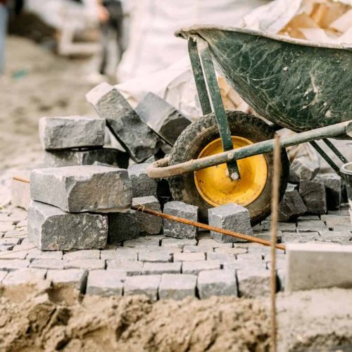 Paving pavement details with granite stones, cobblestock blocks and wheelbarrow on construction site