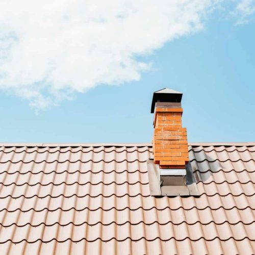 Tiled roof of a house with a brick chimney against a blue cloudy sky during the day. Exterior of a